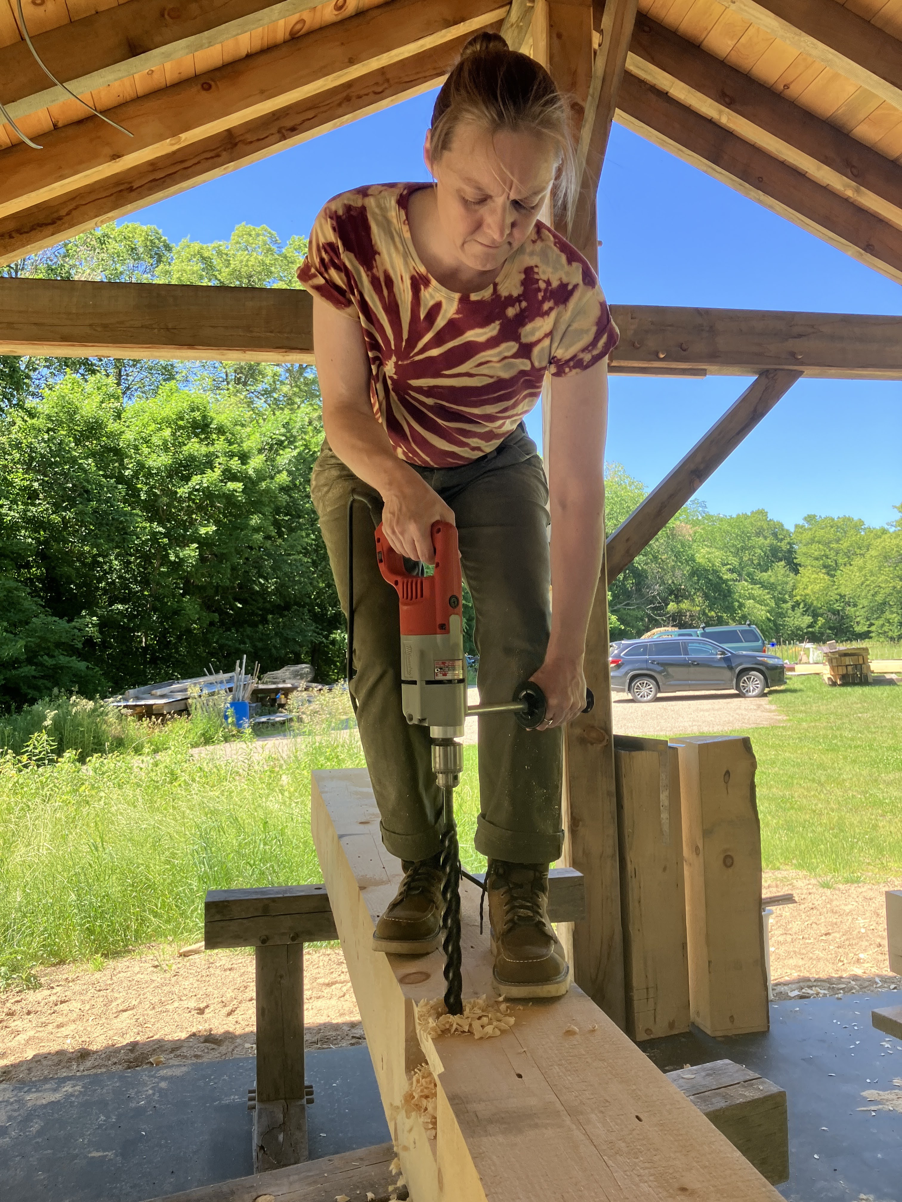 Student of a FLINTA timber framing course and now Timber Club Member, drilling a hole in a timber frame post with a powerdrill.