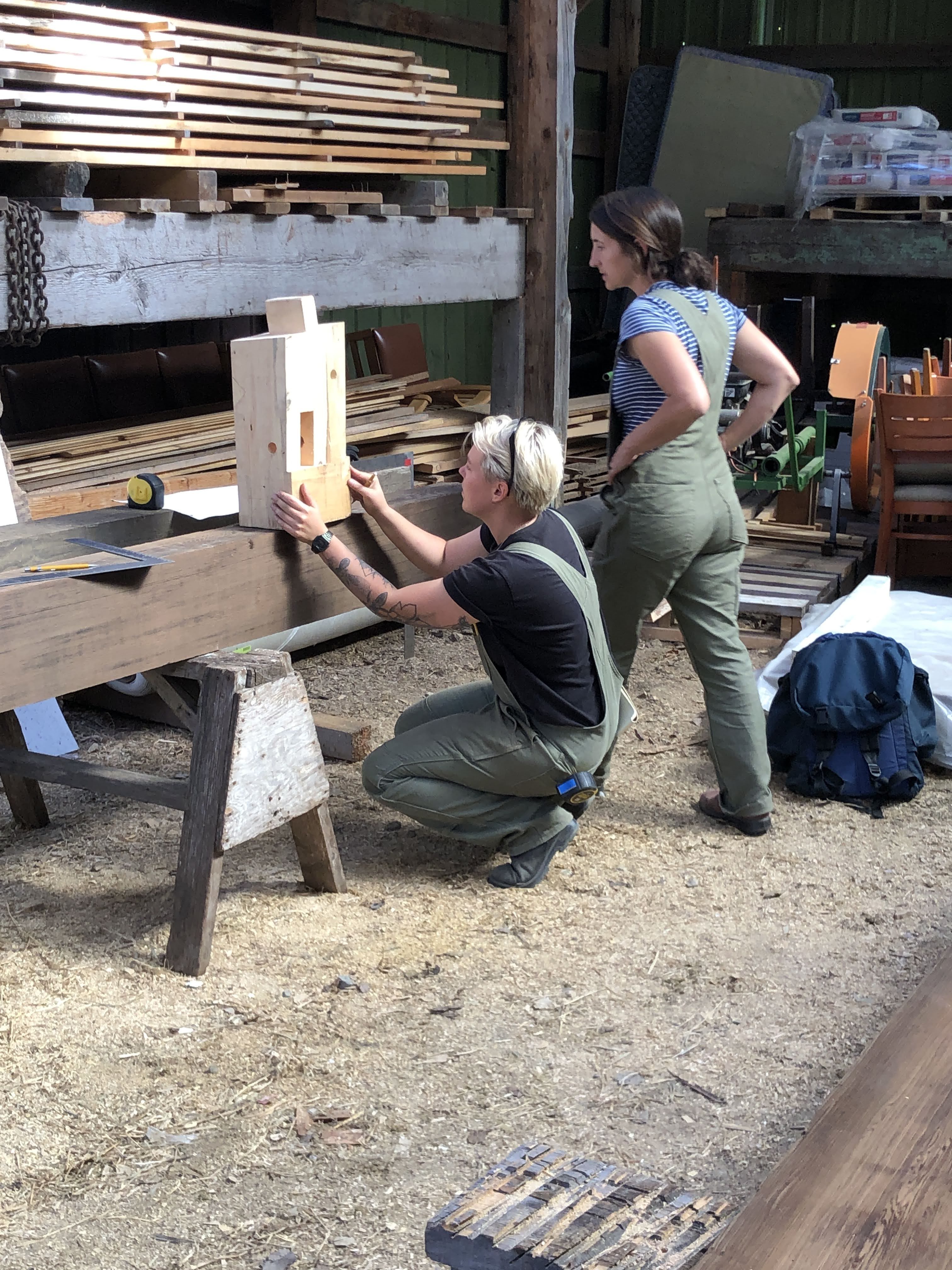 One Founder of Against The Grain - Helen Prüfer - inspecting a timber frame post with a student of a women's timber framing course.